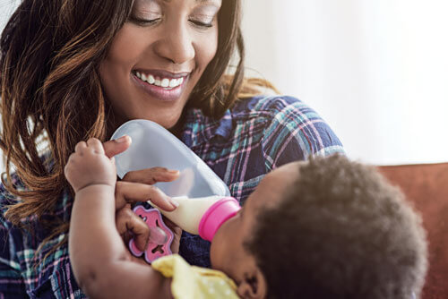Woman smiling while feeding baby with bottle.