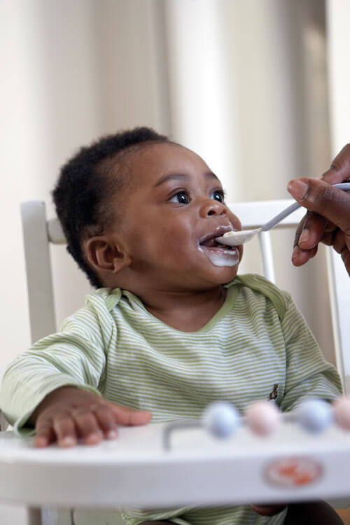 Baby being fed with a spoon, smiling happily.