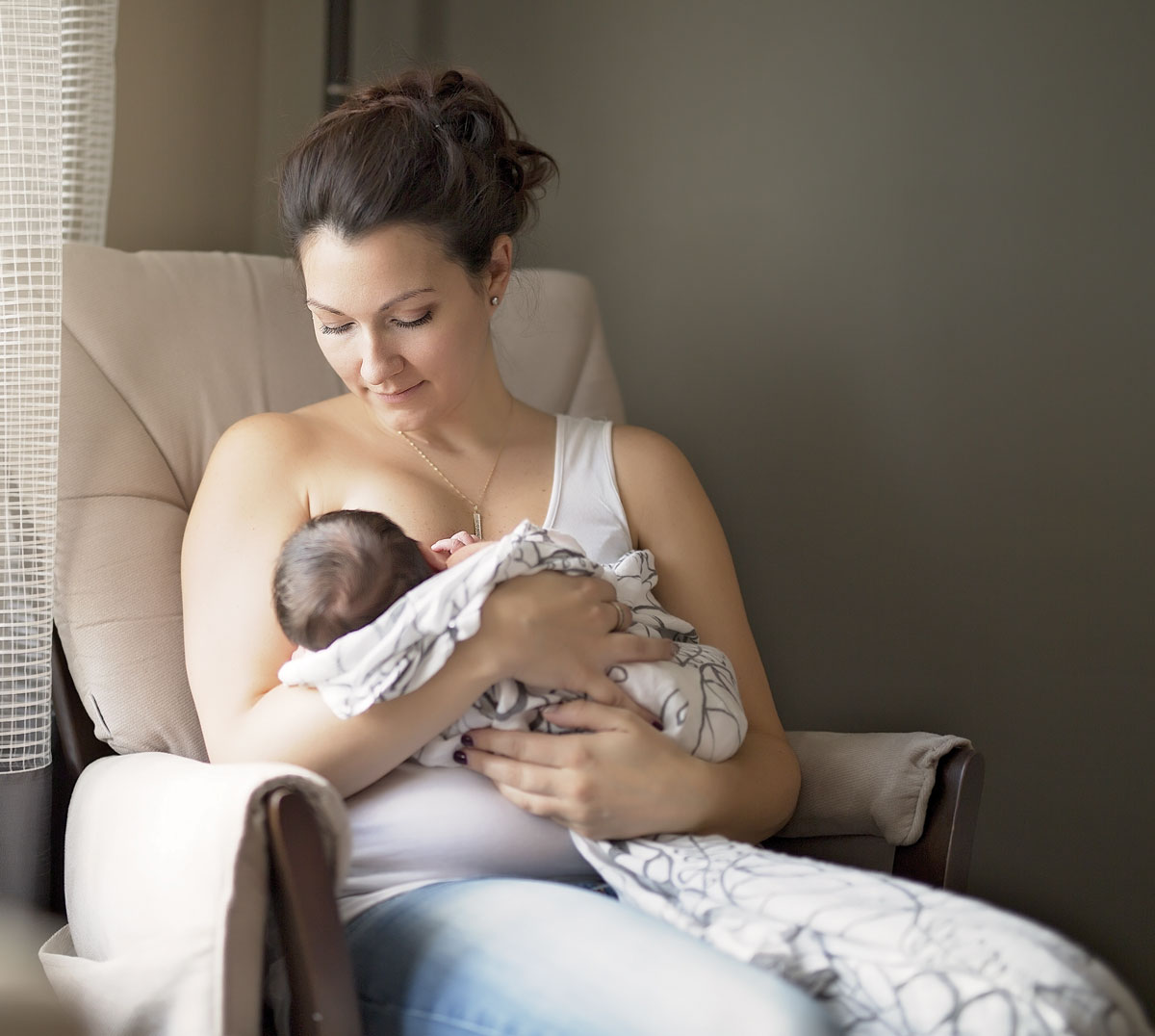 Mother lovingly breastfeeding newborn in cozy chair.