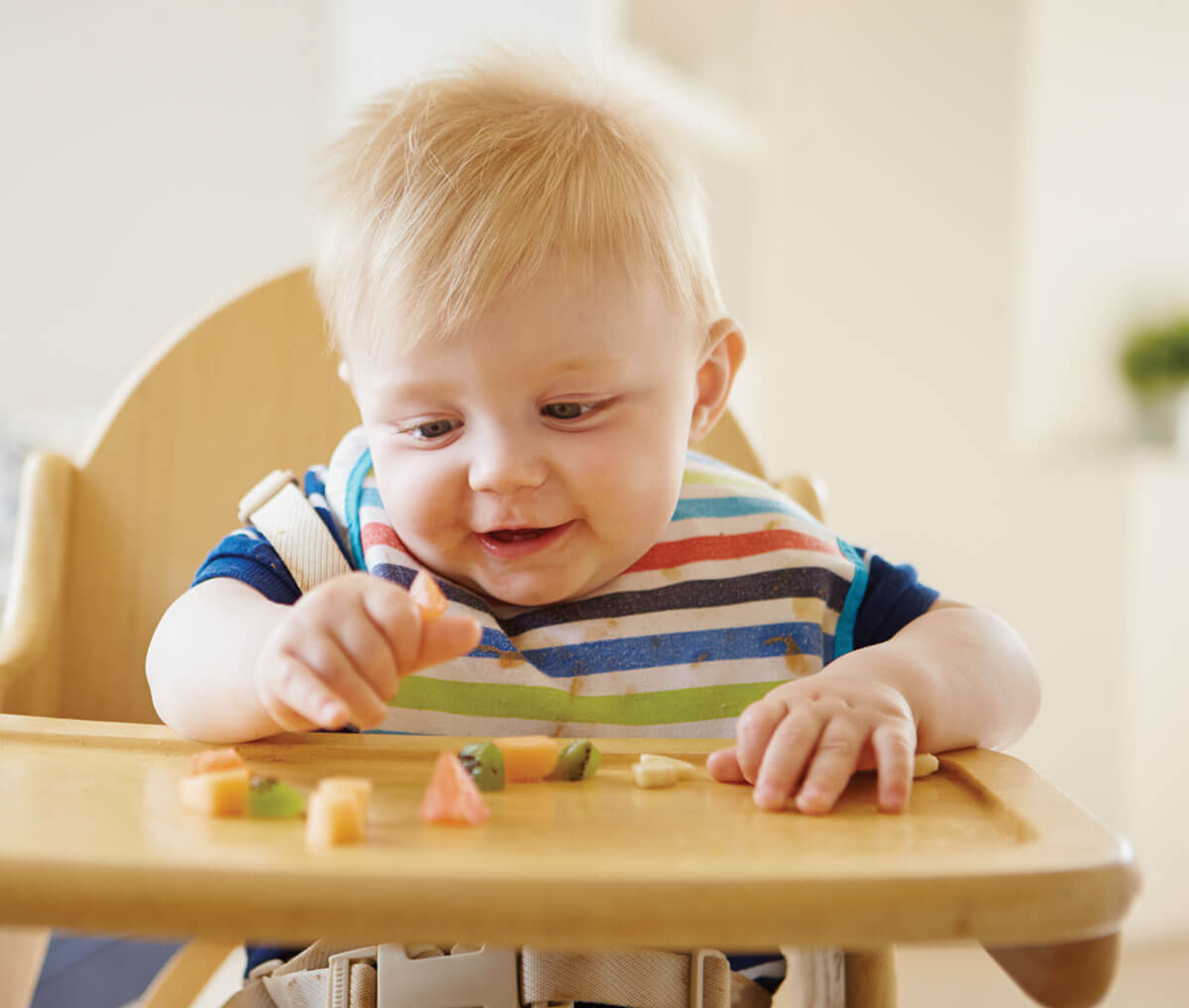 Baby exploring colorful vegetables on highchair tray.