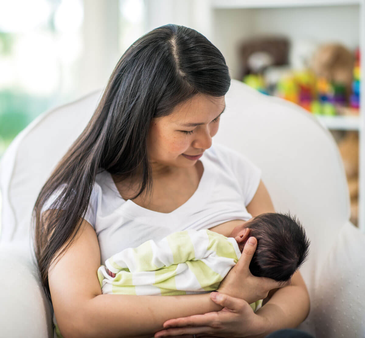 Mother breastfeeding baby in airy, bright room.