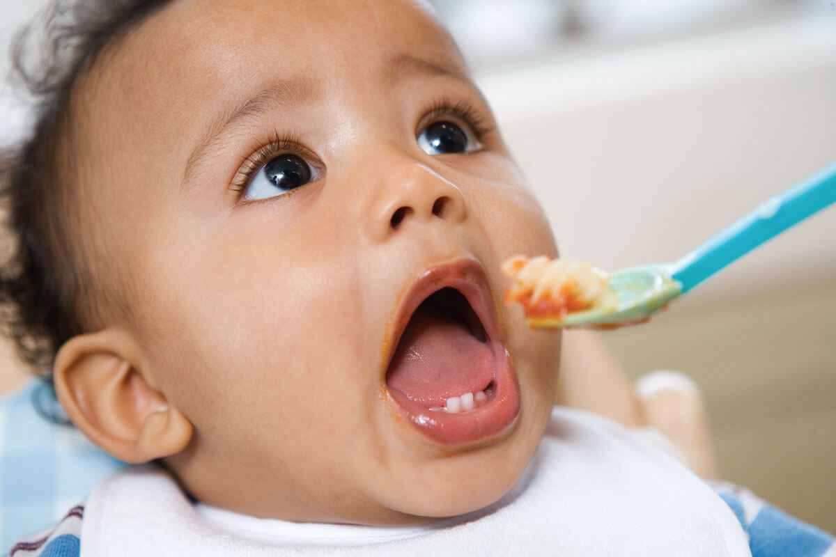 Baby eagerly opening mouth for a spoonful of food.