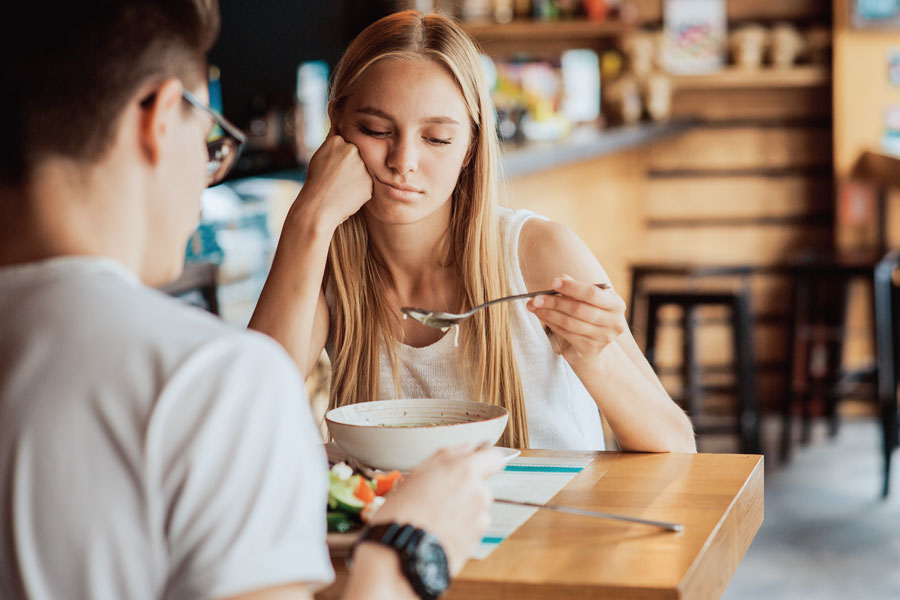 Woman eating soup, appearing uninterested at restaurant table.