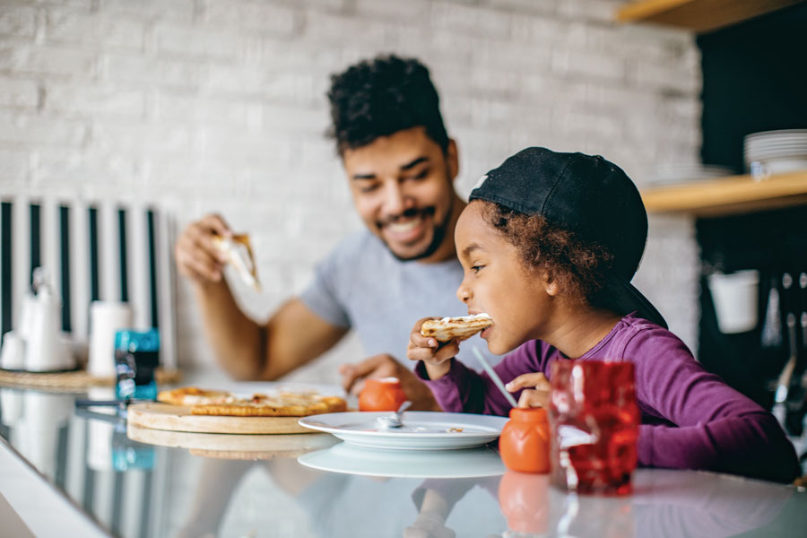 Father and child enjoying pizza together at home.