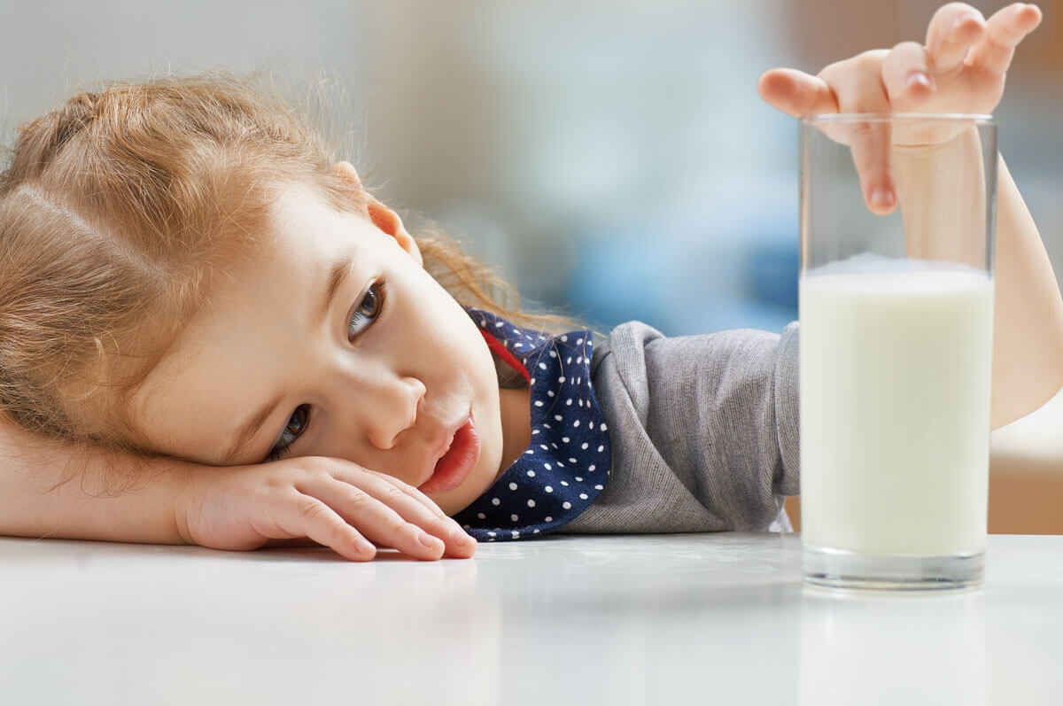 Child reaching for a tall glass of milk.