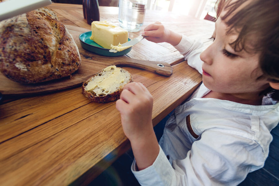 Child spreading butter on a slice of bread.
