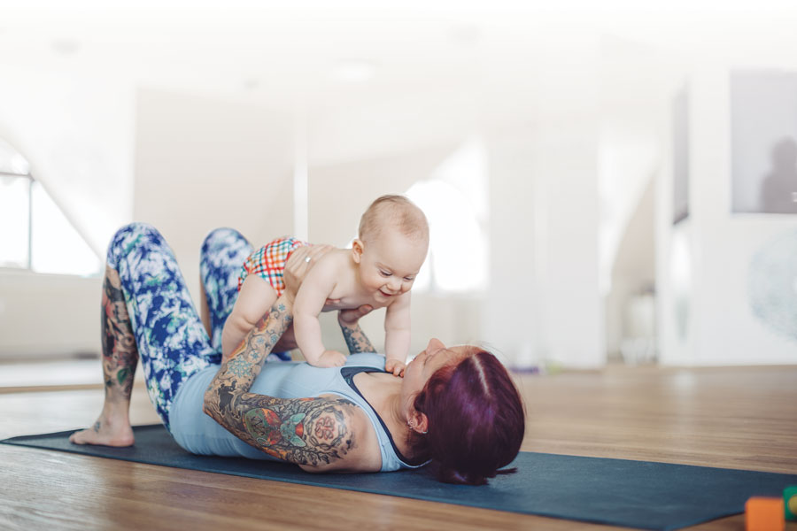 Mother lifting smiling baby during yoga session indoors.