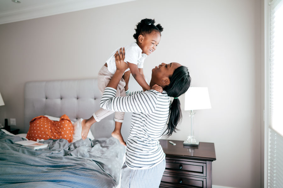 Parent joyfully lifting smiling child in bedroom.