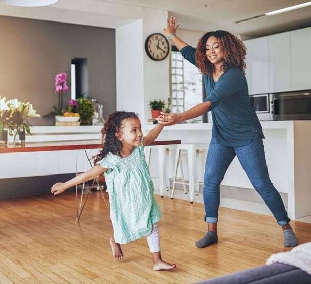 Mother and daughter joyfully dancing in kitchen.
