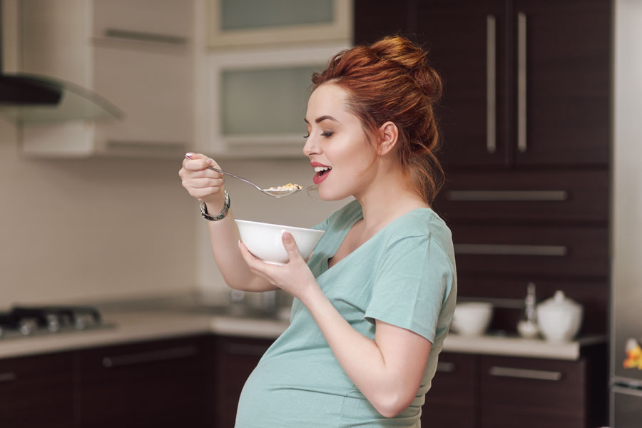 Pregnant woman enjoying cereal in modern kitchen.