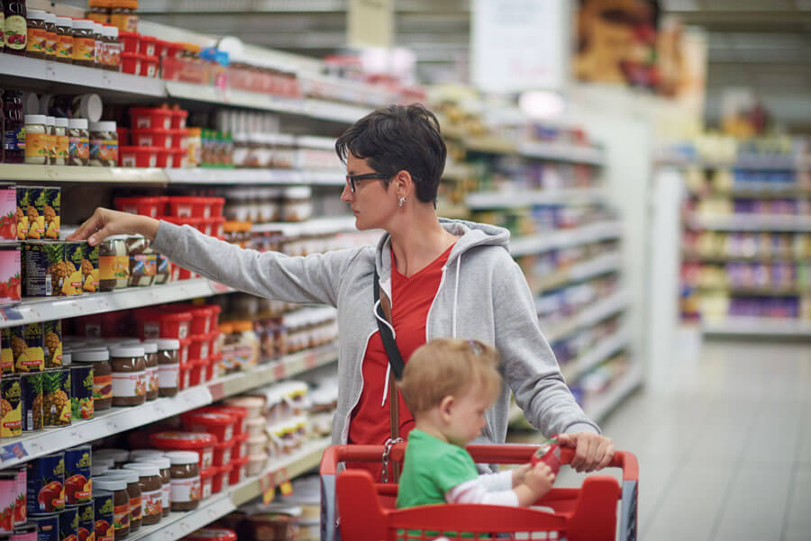 Parent shopping with child in grocery store aisle.