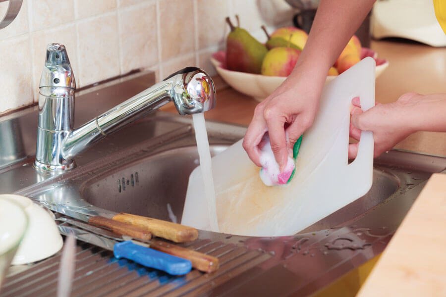 Washing a cutting board under running water.