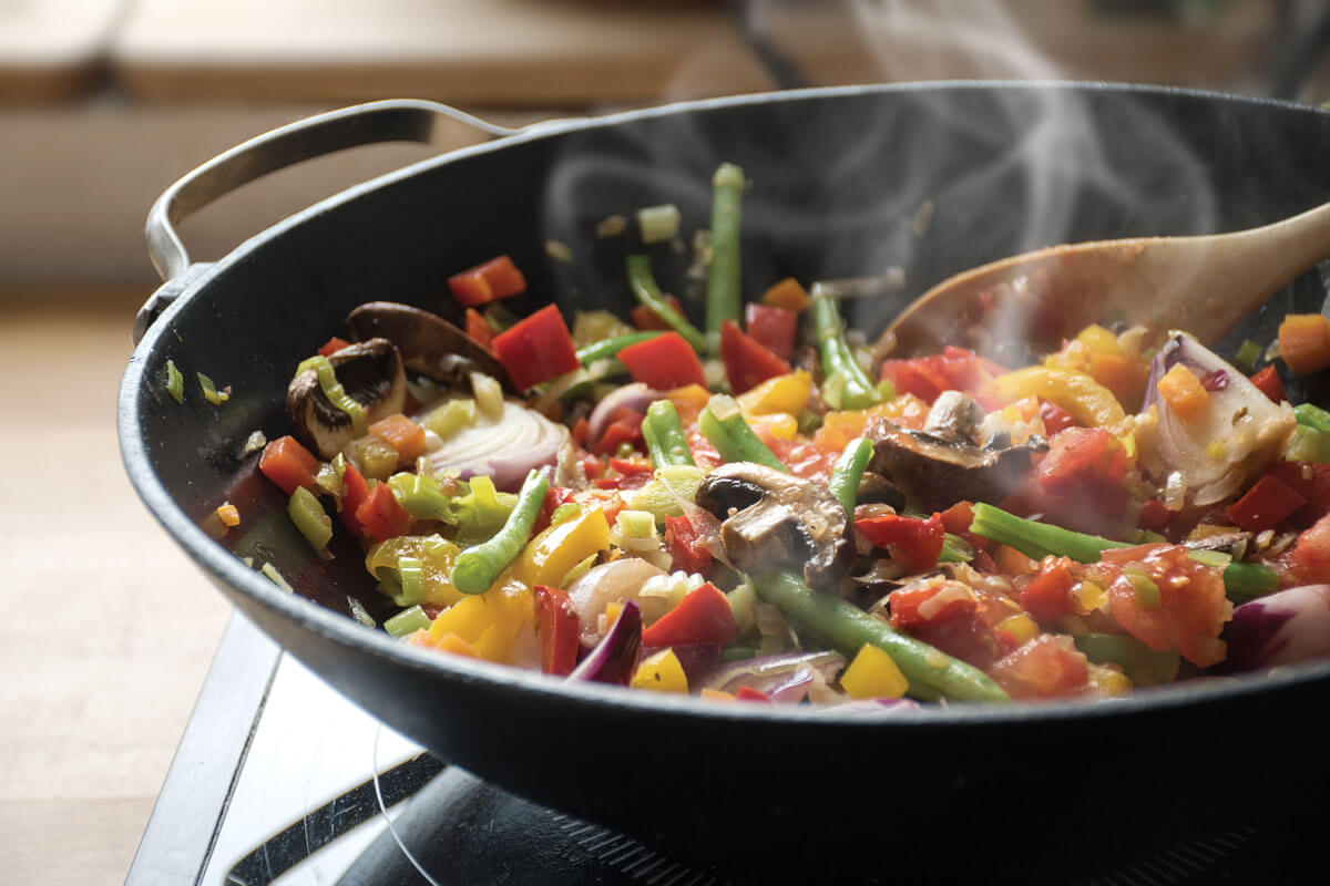 Vegetables sizzling in a pan on stovetop.