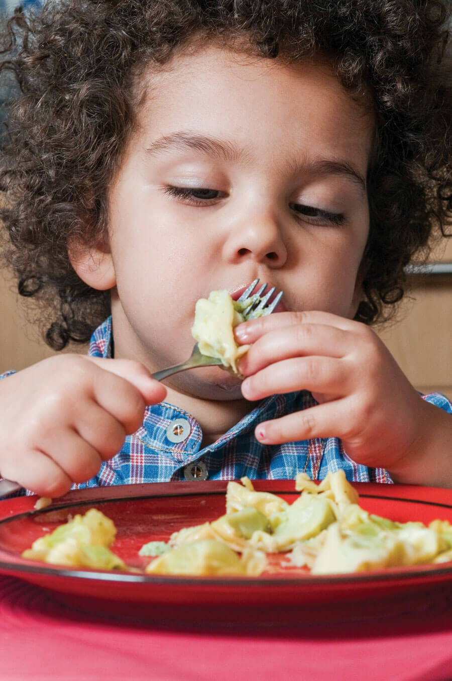 Child eating pasta with a fork.