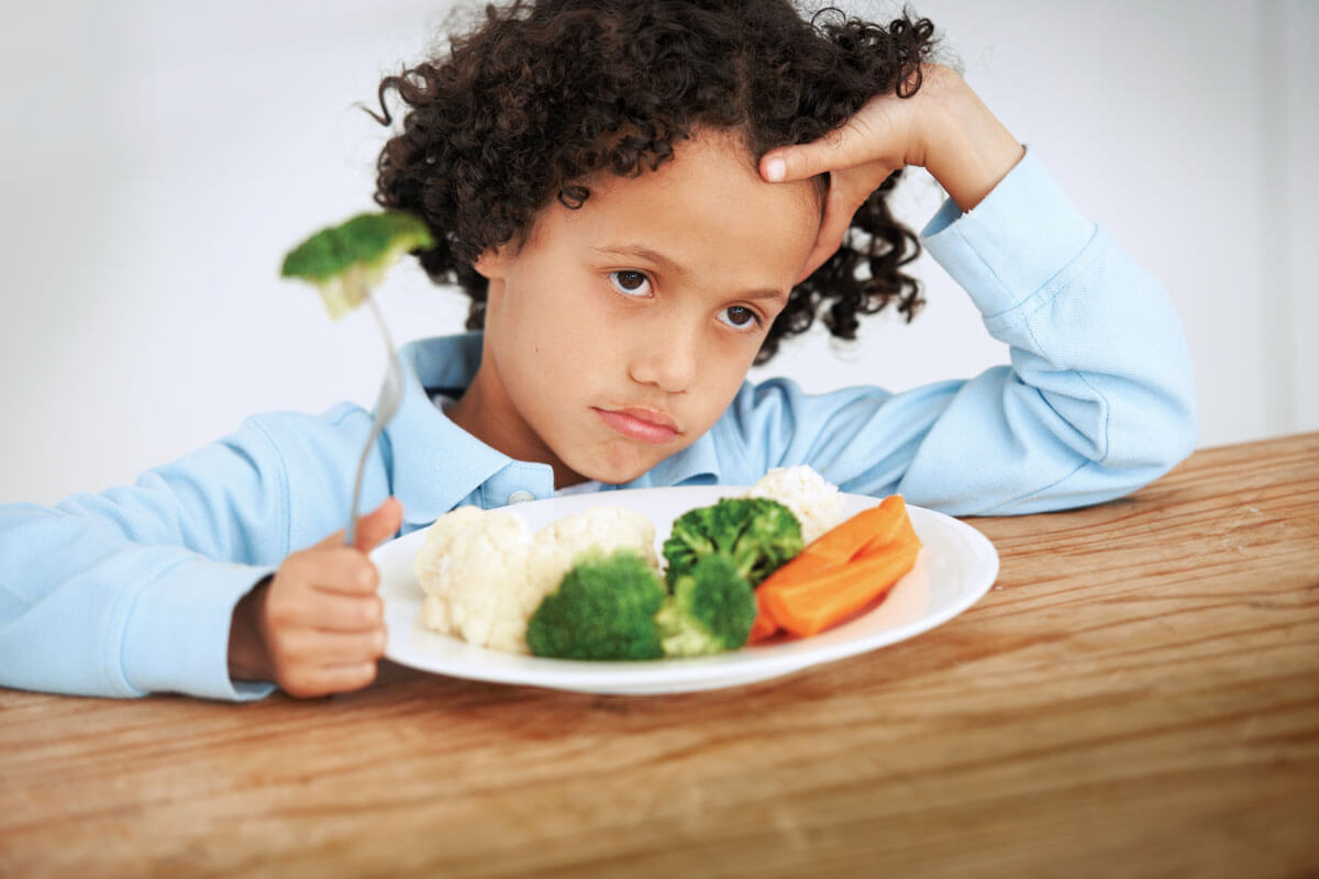 Child uninterested in plate of vegetables, holding fork.