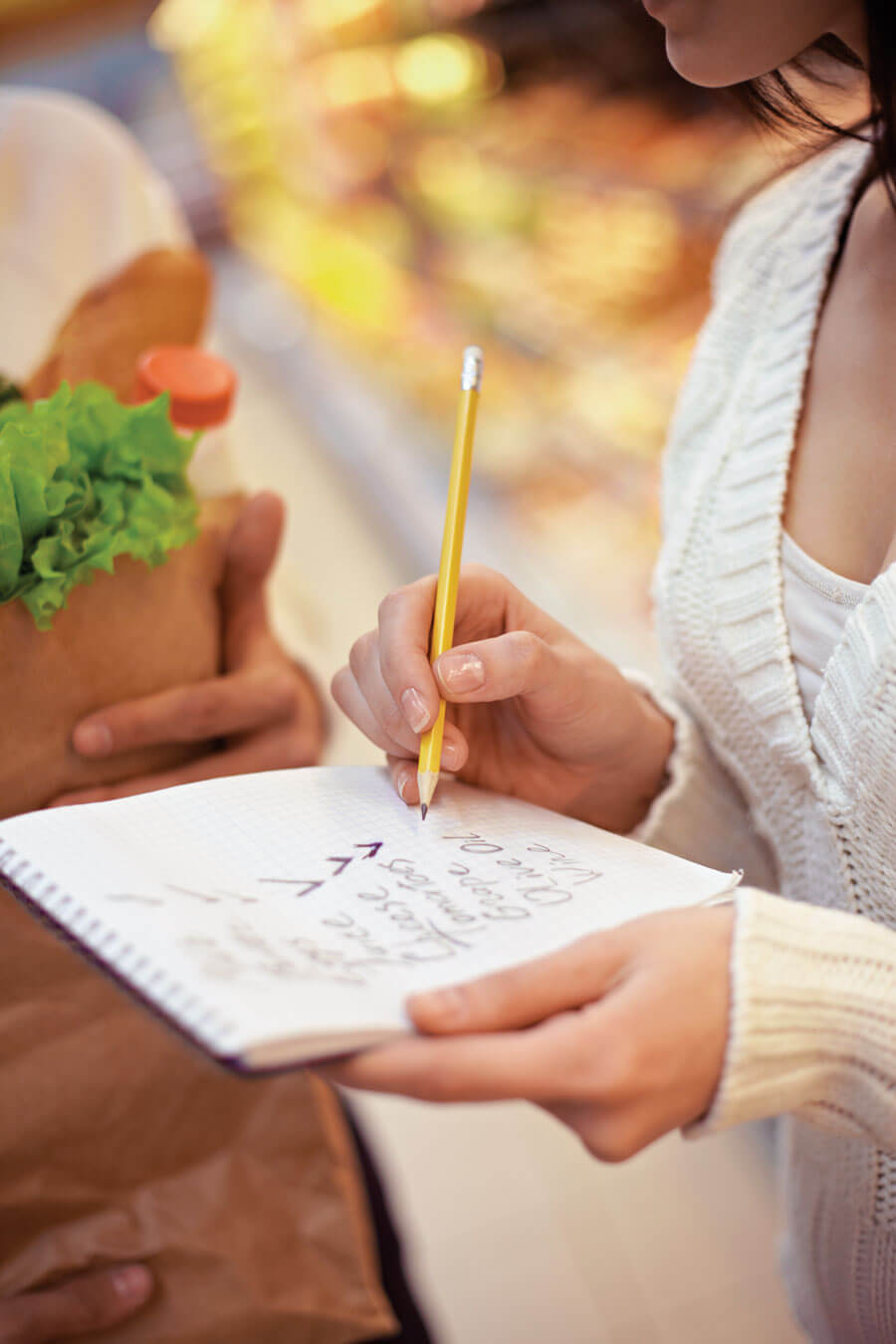 Woman writing grocery list with pencil in store.