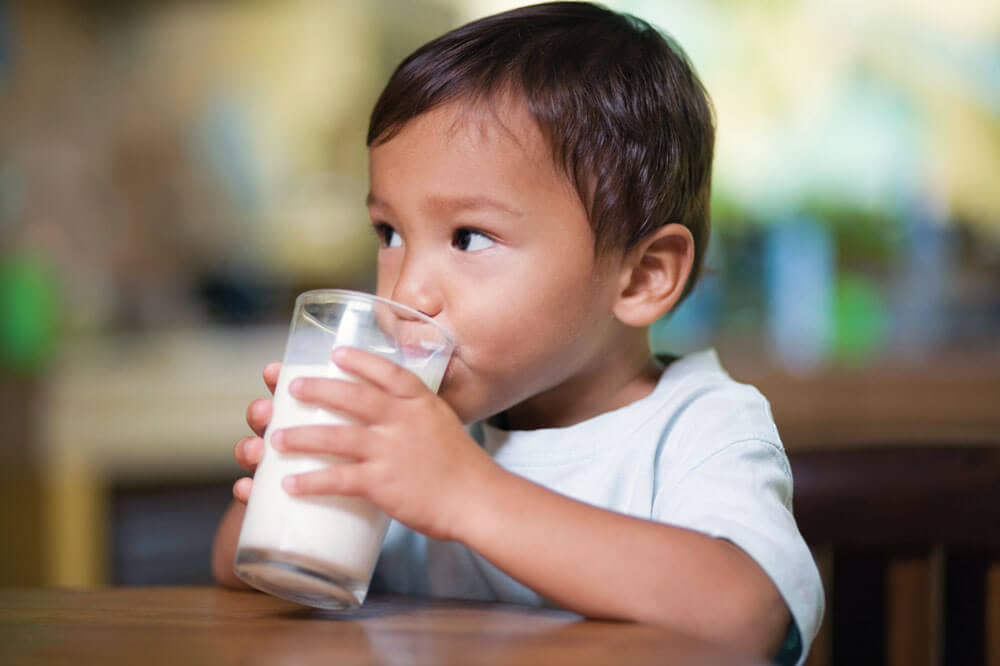 Child drinking milk from a glass at table.
