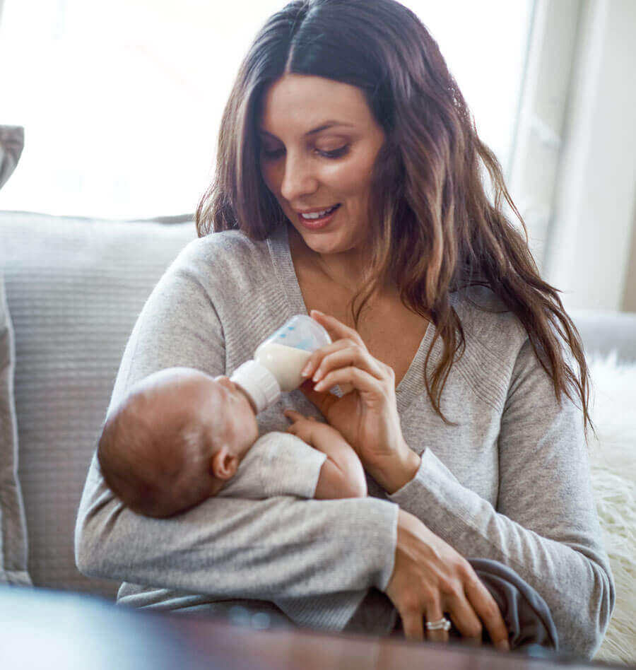 Mother feeding baby with a bottle, smiling warmly.