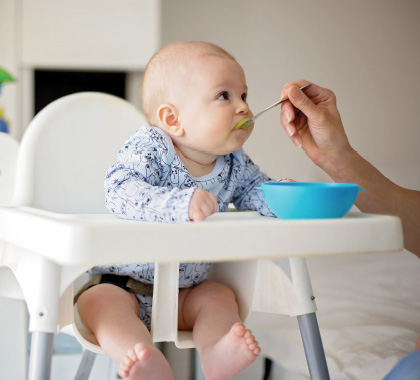 Baby being fed with spoon in high chair.