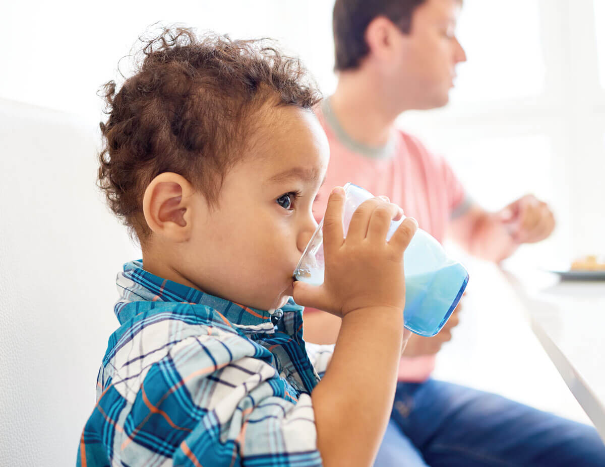 Toddler drinking milk from blue cup at table.