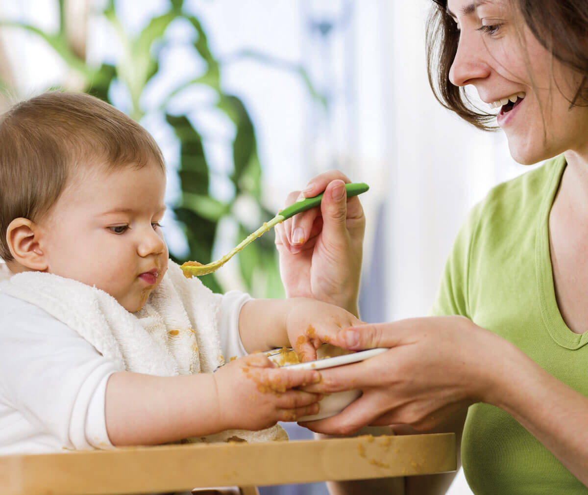 Mother feeding baby pureed food with spoon.