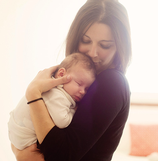 Mother gently holding sleeping baby in her arms.