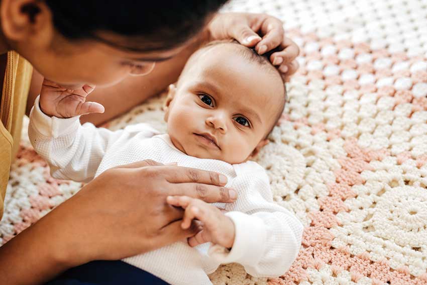 Mother gently cradling baby on crocheted blanket.