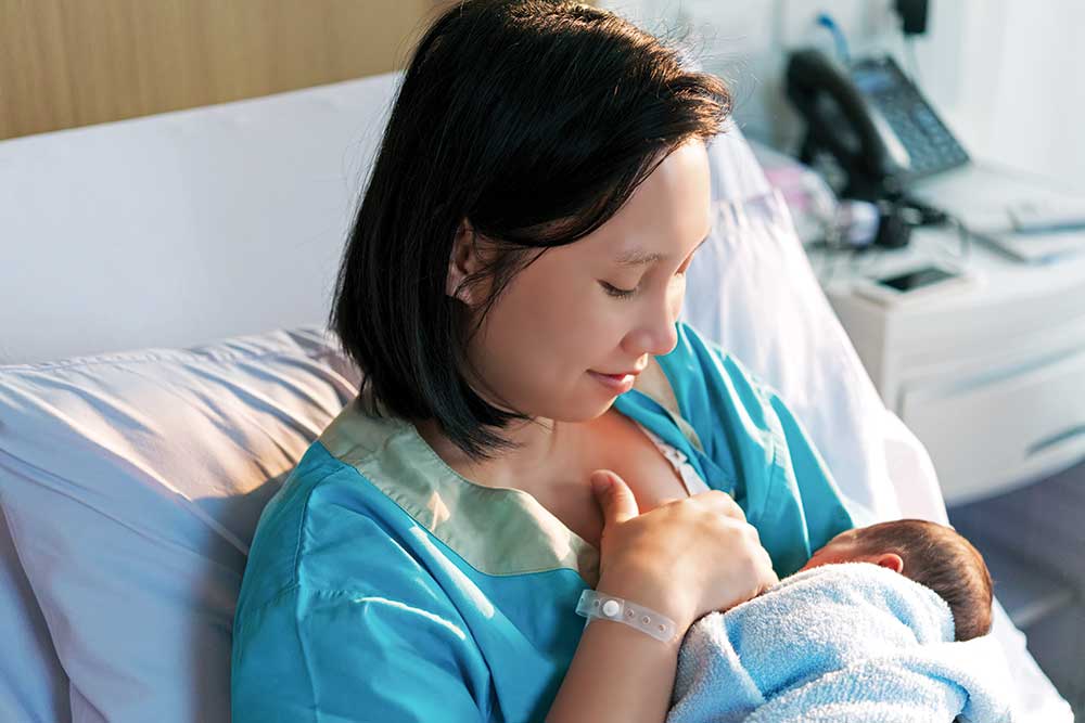 Mother breastfeeding newborn in hospital bed.