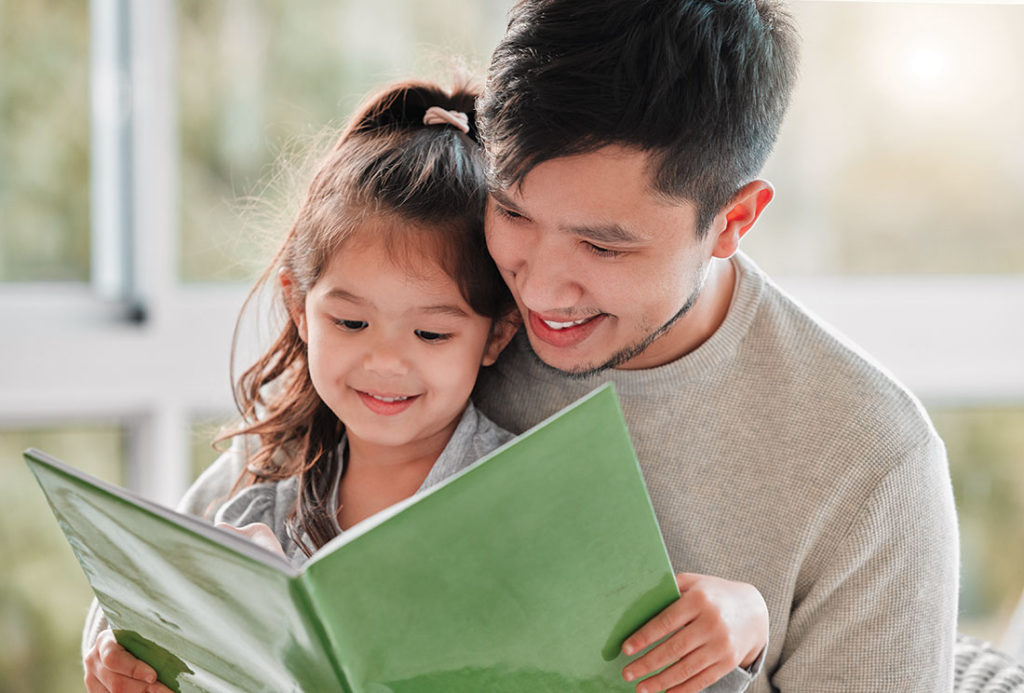 Father and daughter reading a green book together.