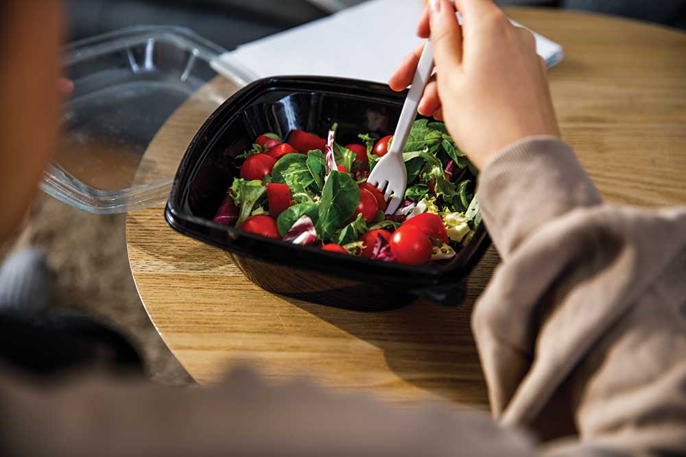 Person eating fresh salad from a black container.