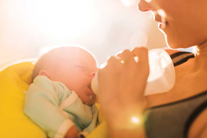 Baby drinking from bottle held by person.