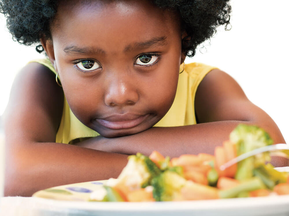 Child gazing at vegetables, arms crossed.