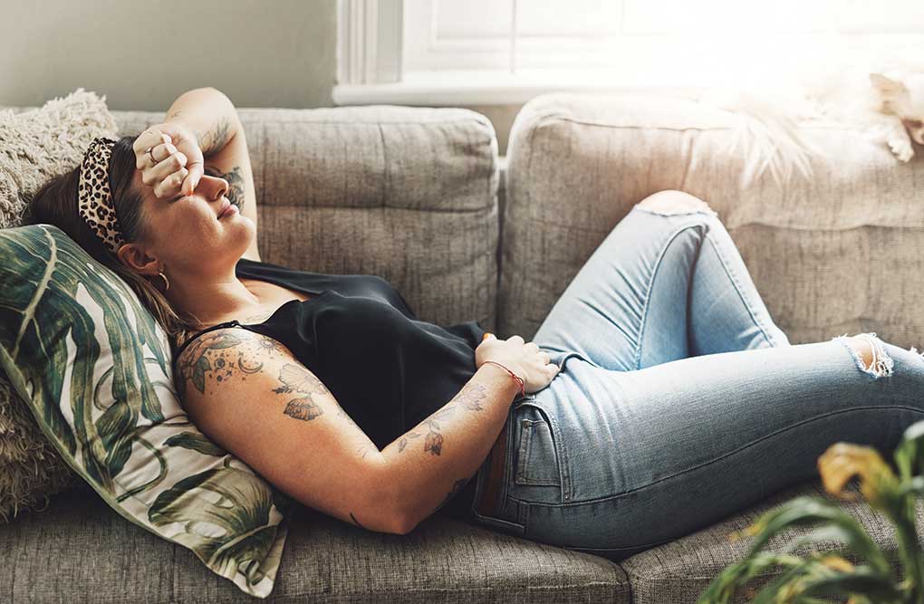 Woman resting on couch, shielding eyes with hand.