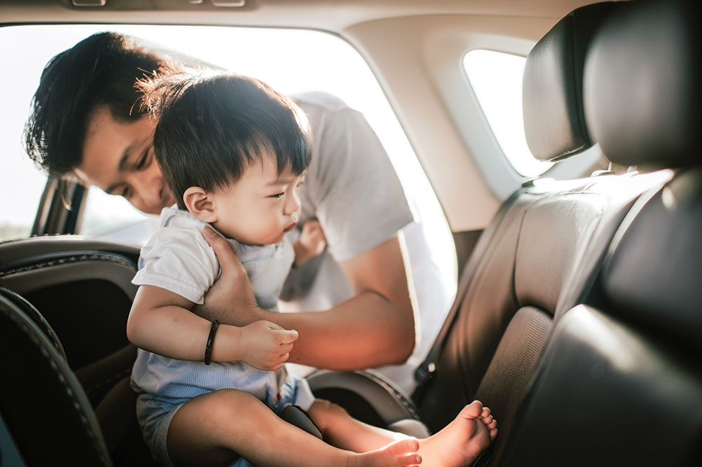 Adult helping child into car seat.
