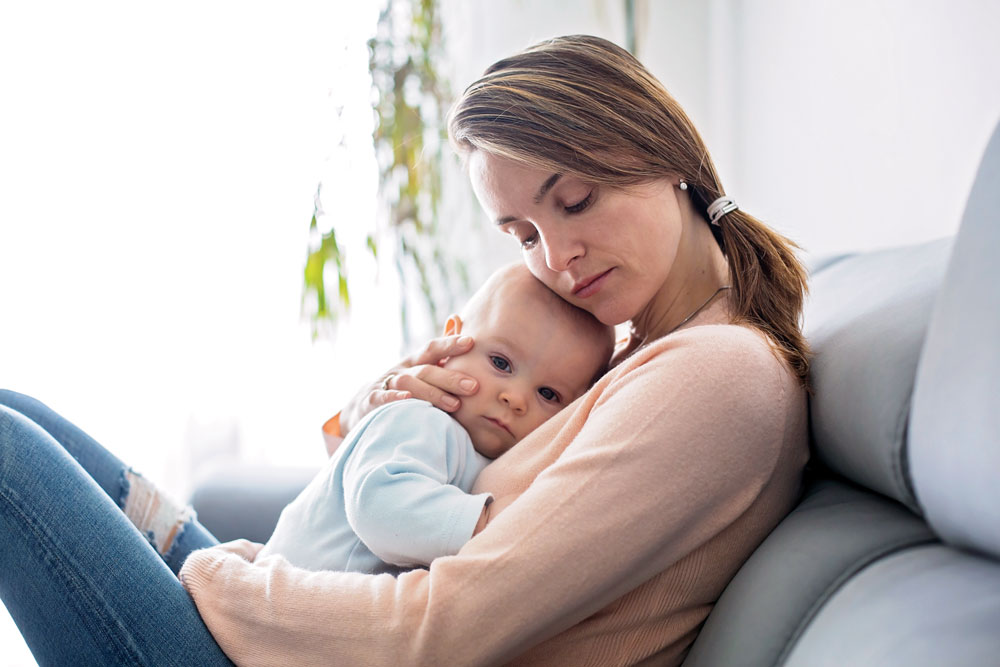 Woman holding baby, sitting on a couch.