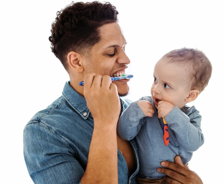 Man and baby brushing teeth, smiling together.