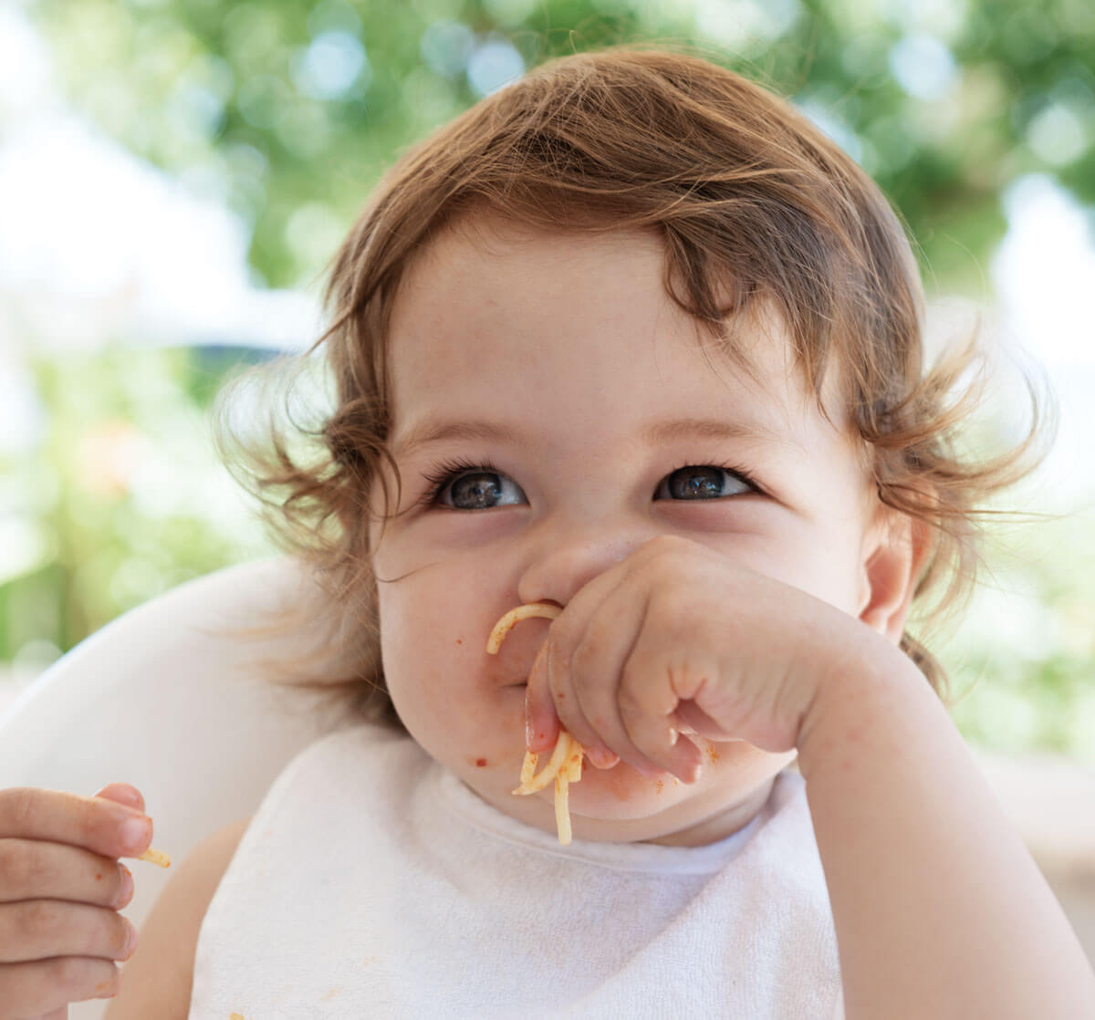 Toddler eating spaghetti with a joyful expression.