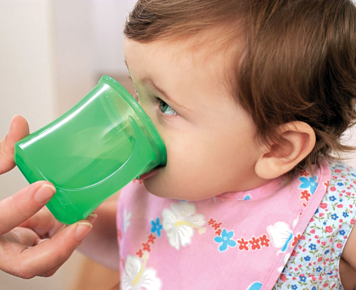 Child drinking from a green cup, wearing a bib.