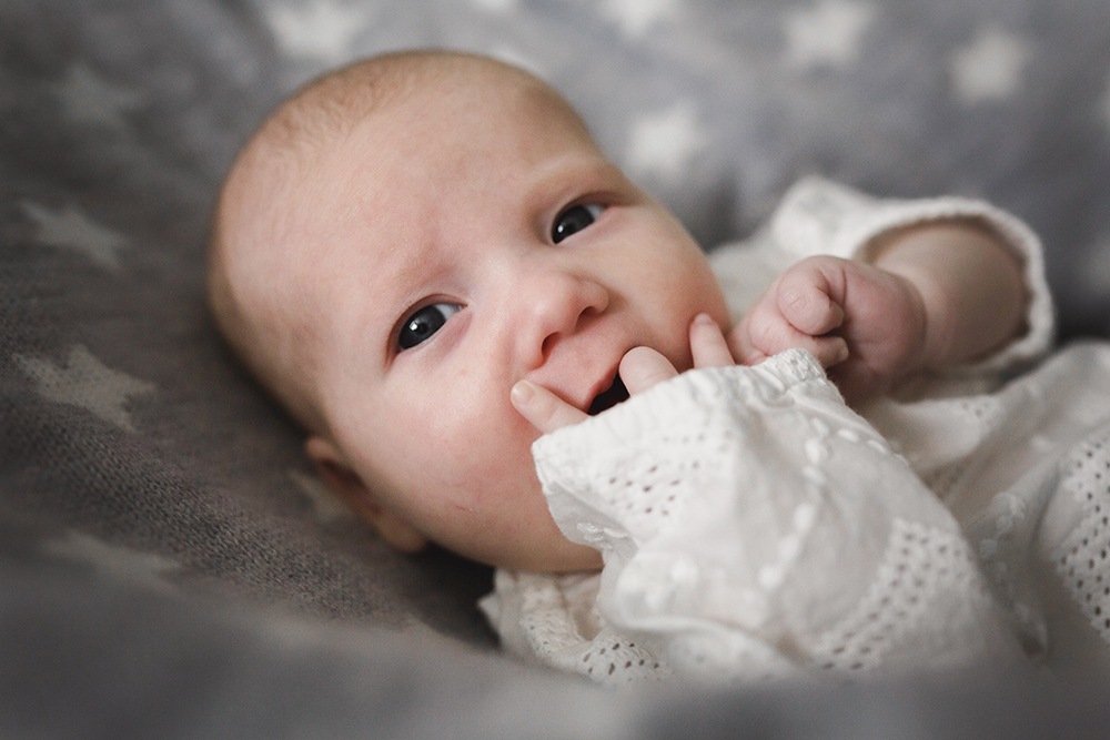 Baby wearing lace, sucking fingers, looking thoughtful.