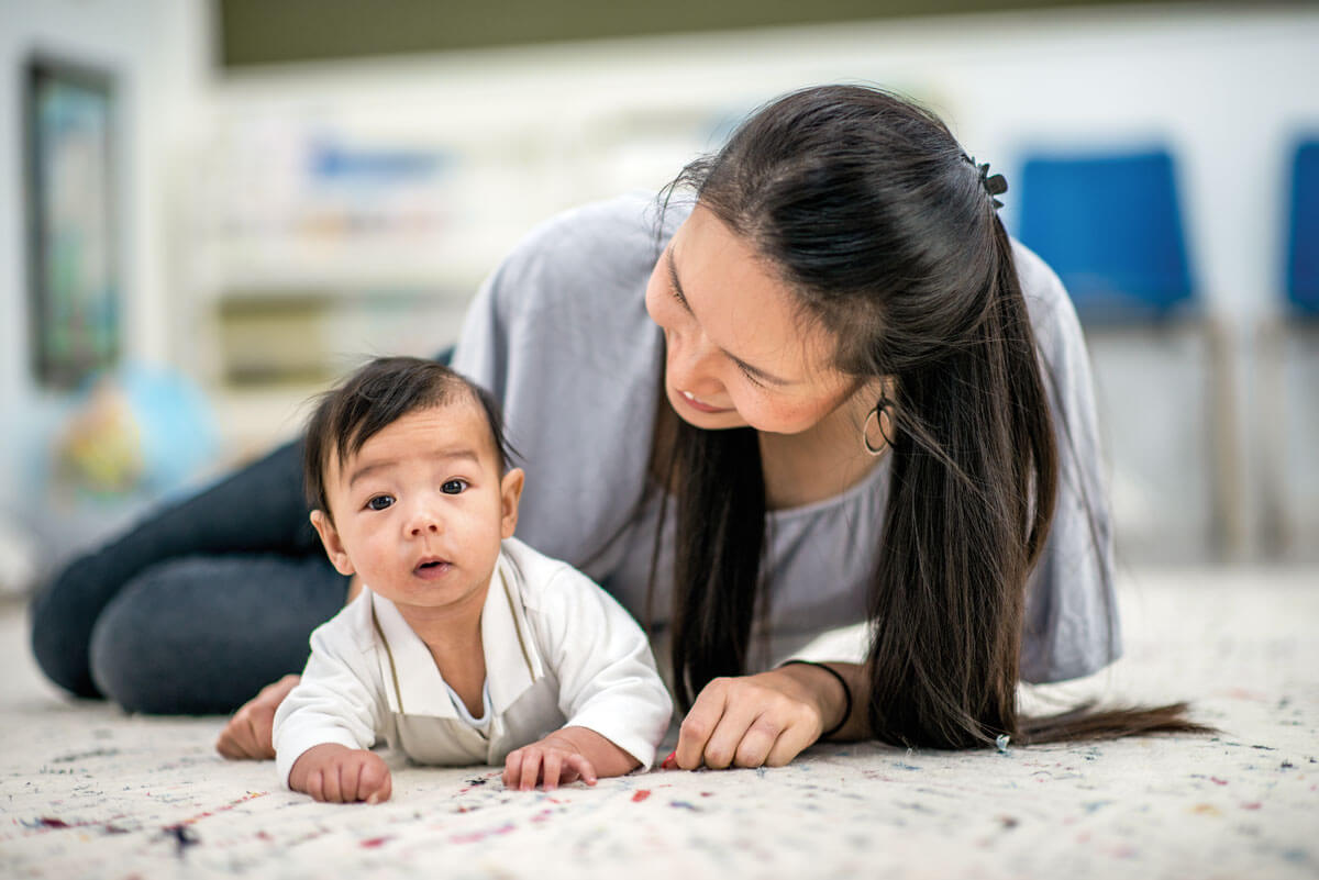 Baby lying on floor, woman smiling nearby.