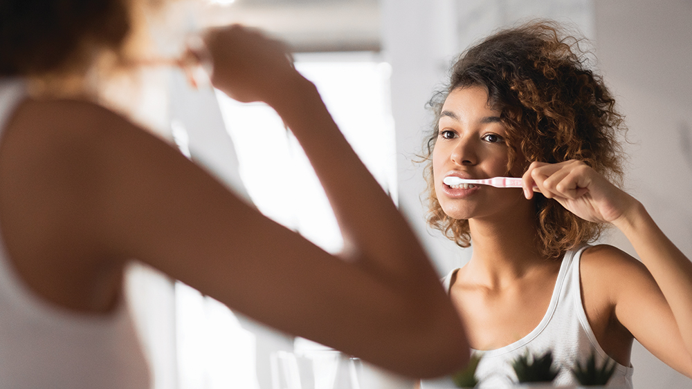 Woman brushing teeth in front of mirror.
