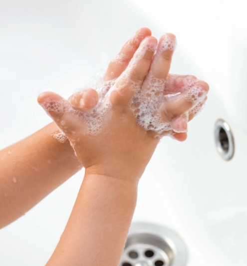 Child washing hands with soap in sink.