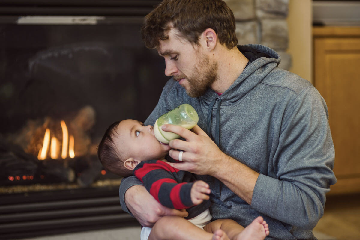 Father bottle-feeding baby by cozy fireplace.