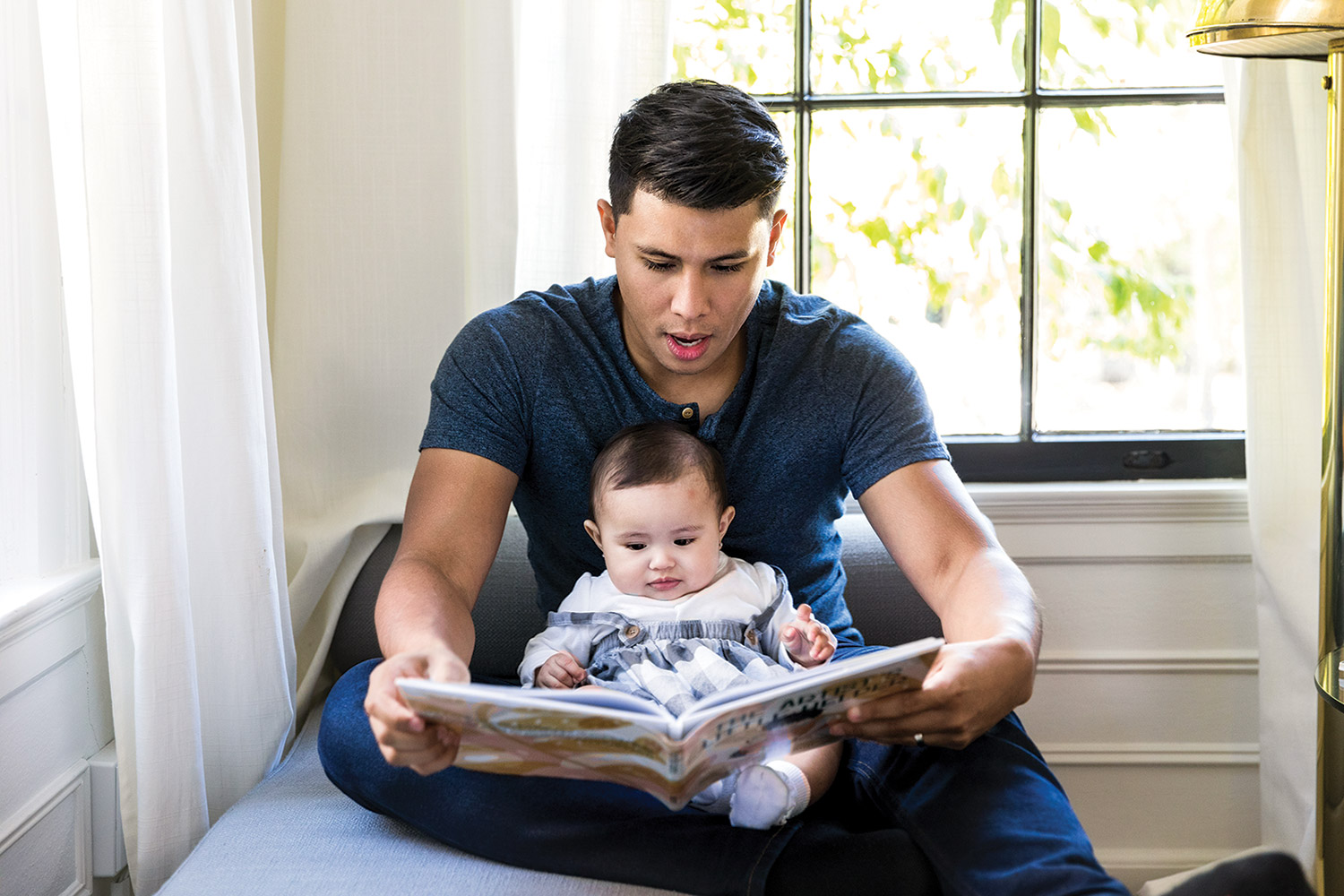 Father reading book with baby on lap indoors.
