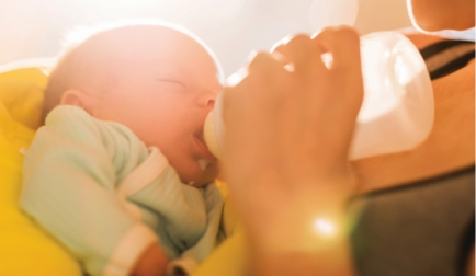 Baby drinking from bottle, held in arms.