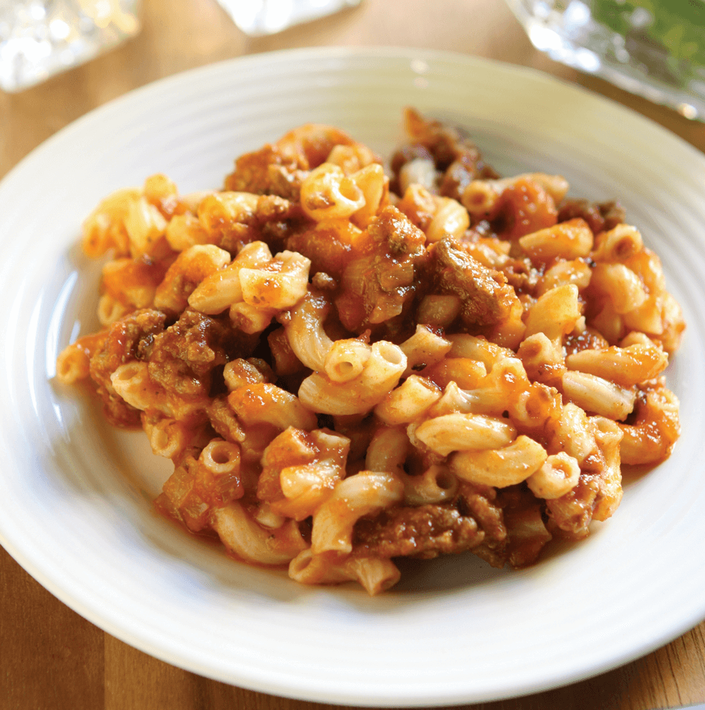 Plate of macaroni with meat sauce on table.