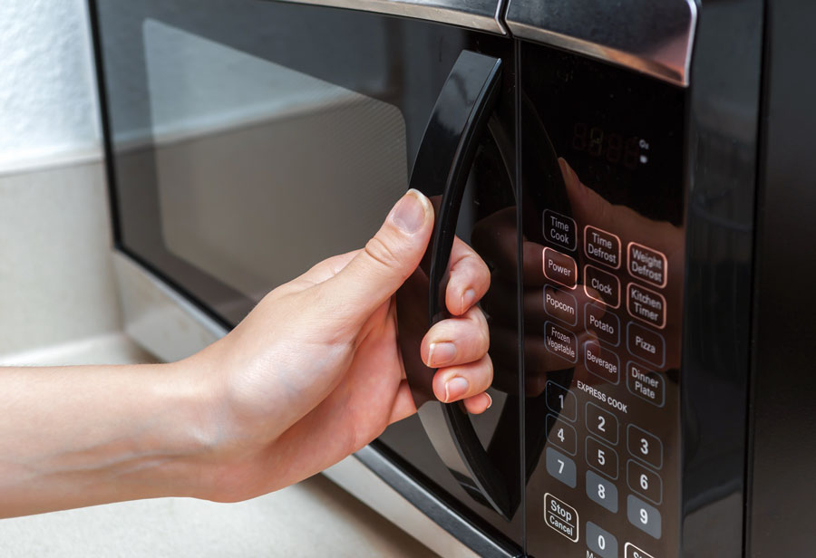 Hand opening black microwave on kitchen counter.