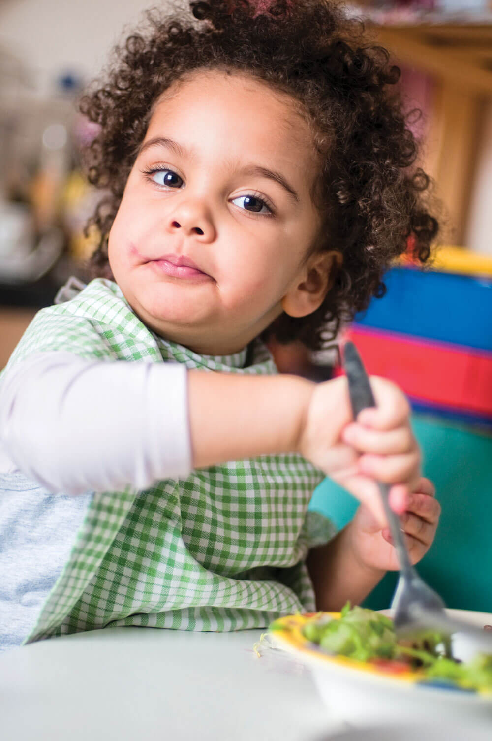 Child eating salad with a fork, wearing bib.