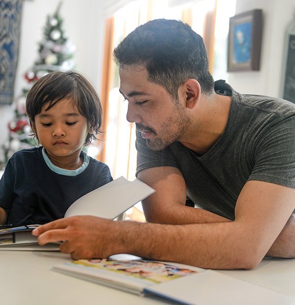 Child and adult reading book together at home.