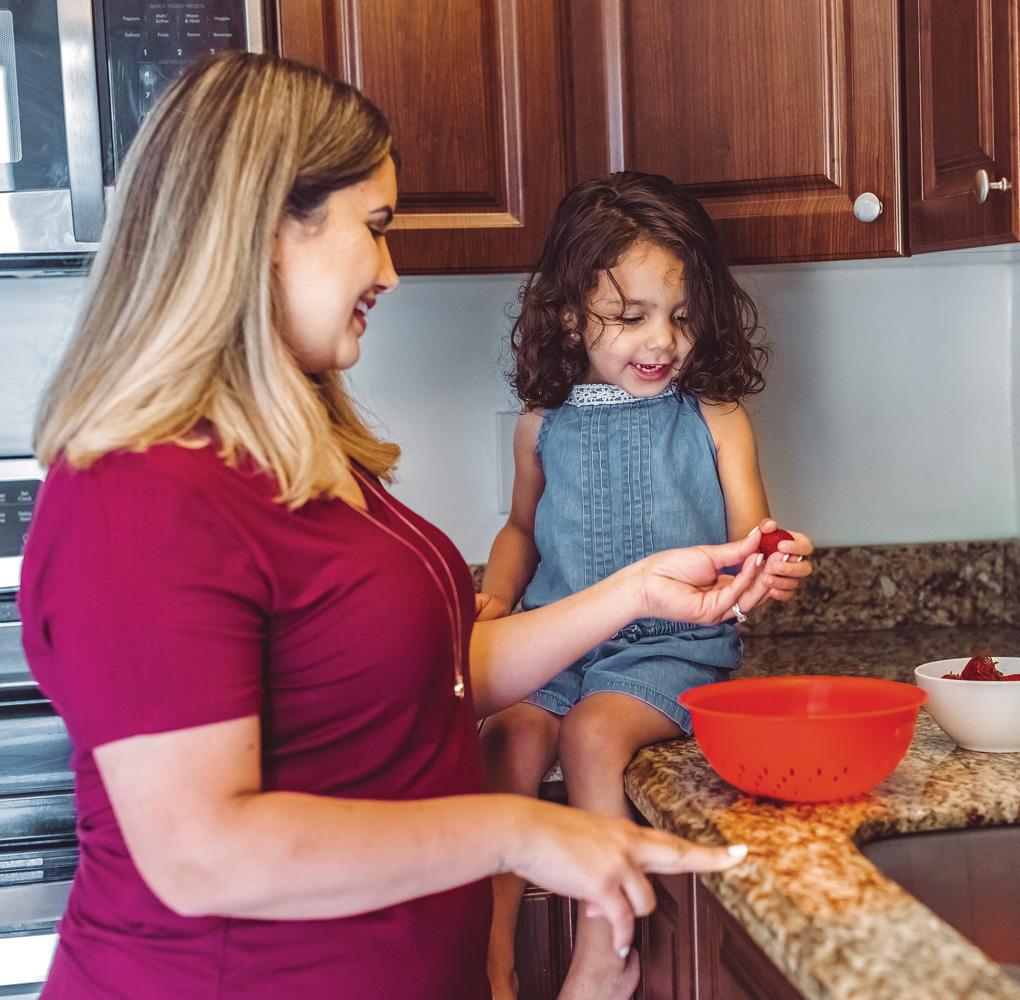 Woman and child smiling, preparing strawberries in kitchen.